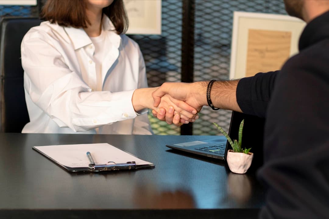 Recruiter shaking hands with a candidate over a resume and laptop